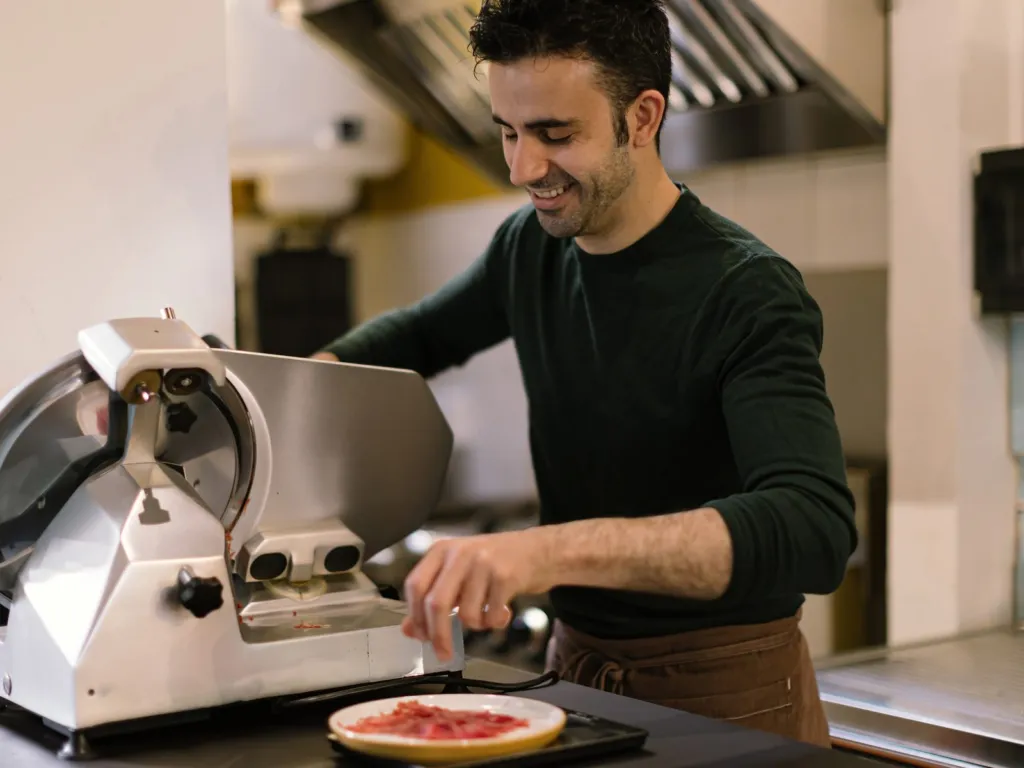 Chef slicing cured meat on a commercial slicer